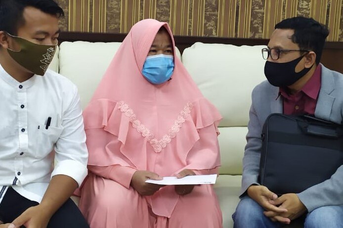 A woman wearing a mask sits on a couch beside two men wearing masks