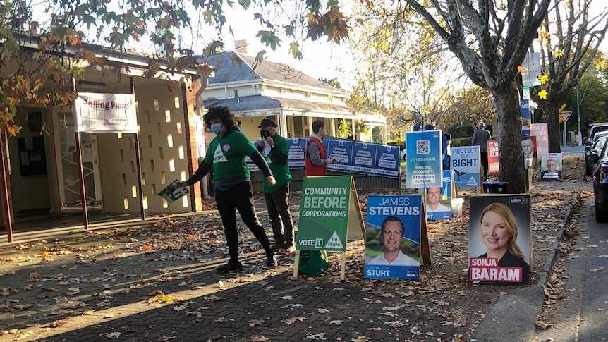 Posters and people handing out how to vote cards at a hall among trees
