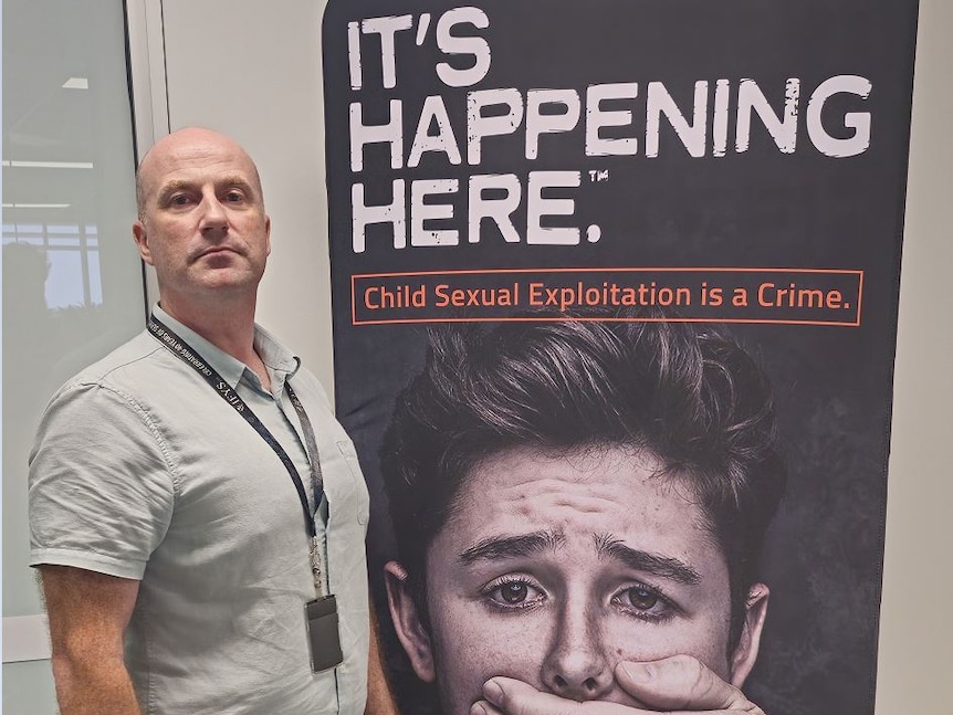 Man standing next to large anti-abuse poster 