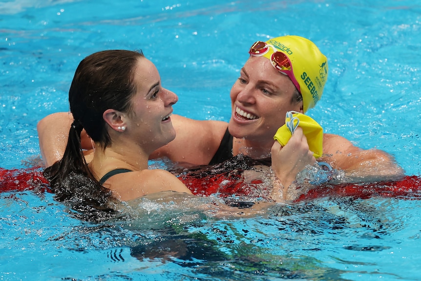 A brunette woman swimming next to another woman wearing a yellow swimming camp