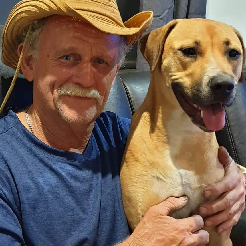 A man wearing a straw hat hugs a dog on a couch.