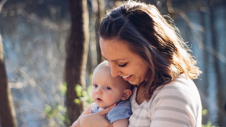 a woman holds a happy little baby in the sunshine