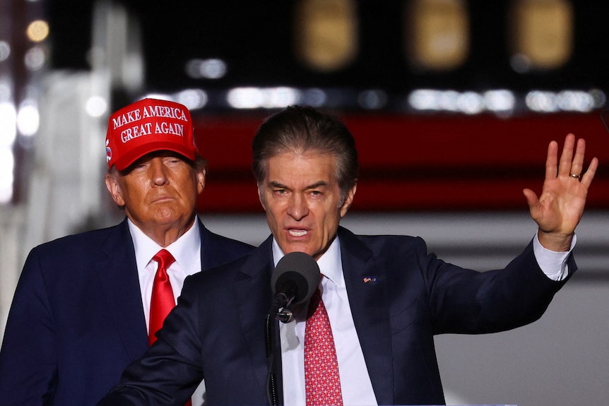 Donald Trump stands behind Dr Oz wearing a Make America Great Again hat