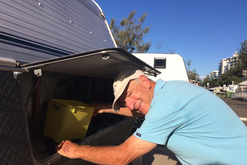 Man puts items away into the rear of the caravan while looking at the camera and smiling.