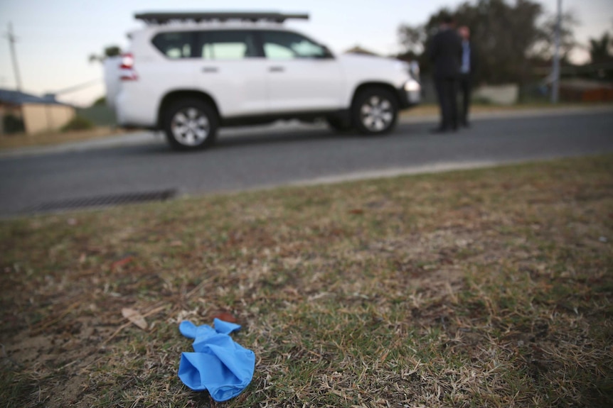 A blue glove on the ground outside a house on Manapouri Meander in Joondalup with a white 4WD and two men in the background.