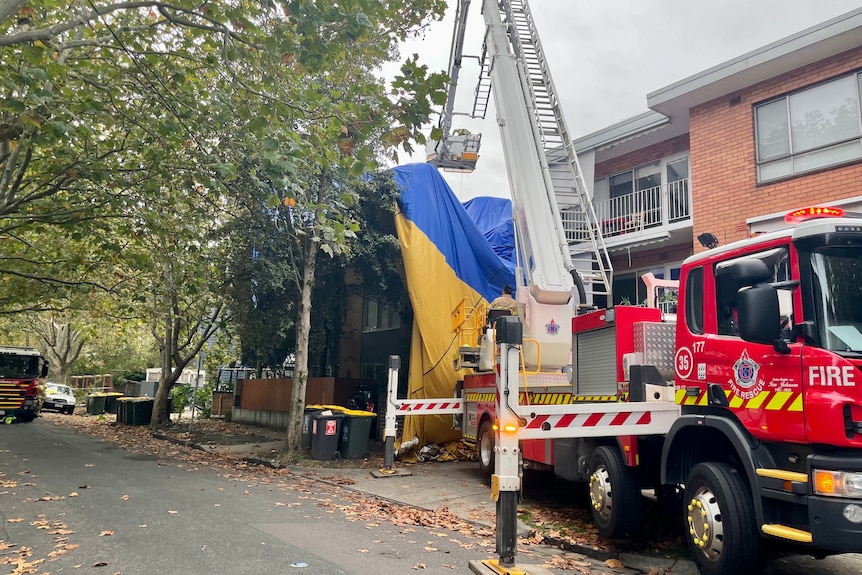 A firetruck attending to a hot air balloon draped over a building