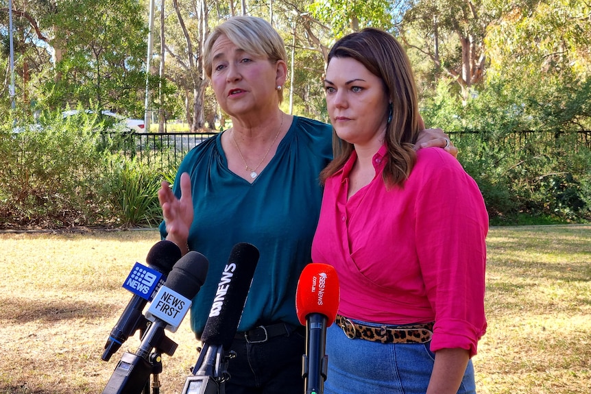 Two women speaking in front of microphones in a park