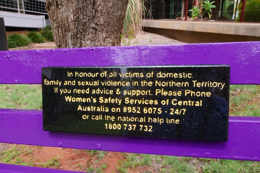 A plaque on a bright purple park bench honours victims of domestic violence and lists support numbers.