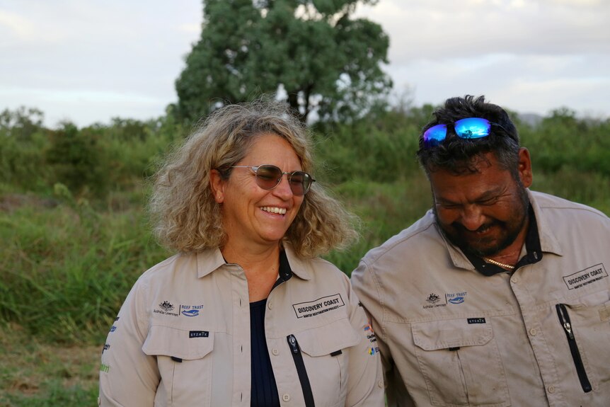 Two Indigenous rangers stand side-by-side and laugh. 