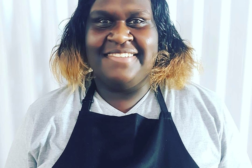 Naz Wapau smiles at the camera wearing a black "Second Shot" apron.