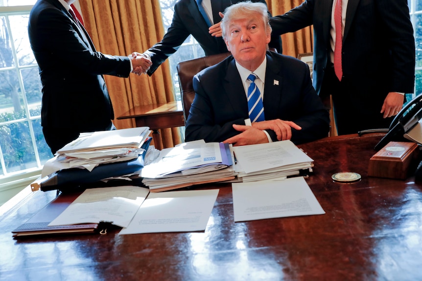 Donald Trump sits at his desk surrounded by documents.