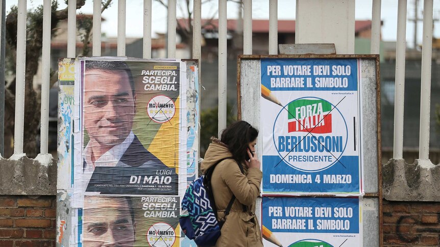 A woman walks past election posters in Italy