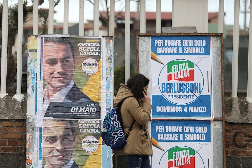 A woman walks past election posters in Italy