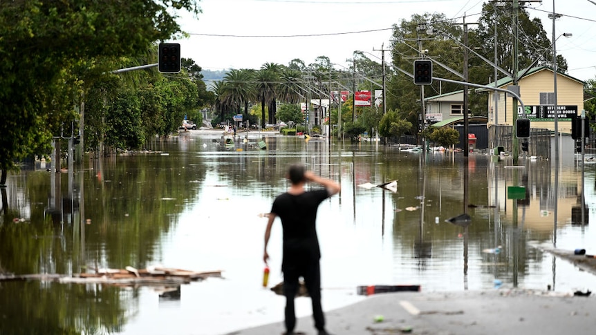 A man looks down a flooded street in Lismore