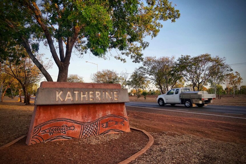A car drives down a road. On the roadside is a sign saying Katherine.
