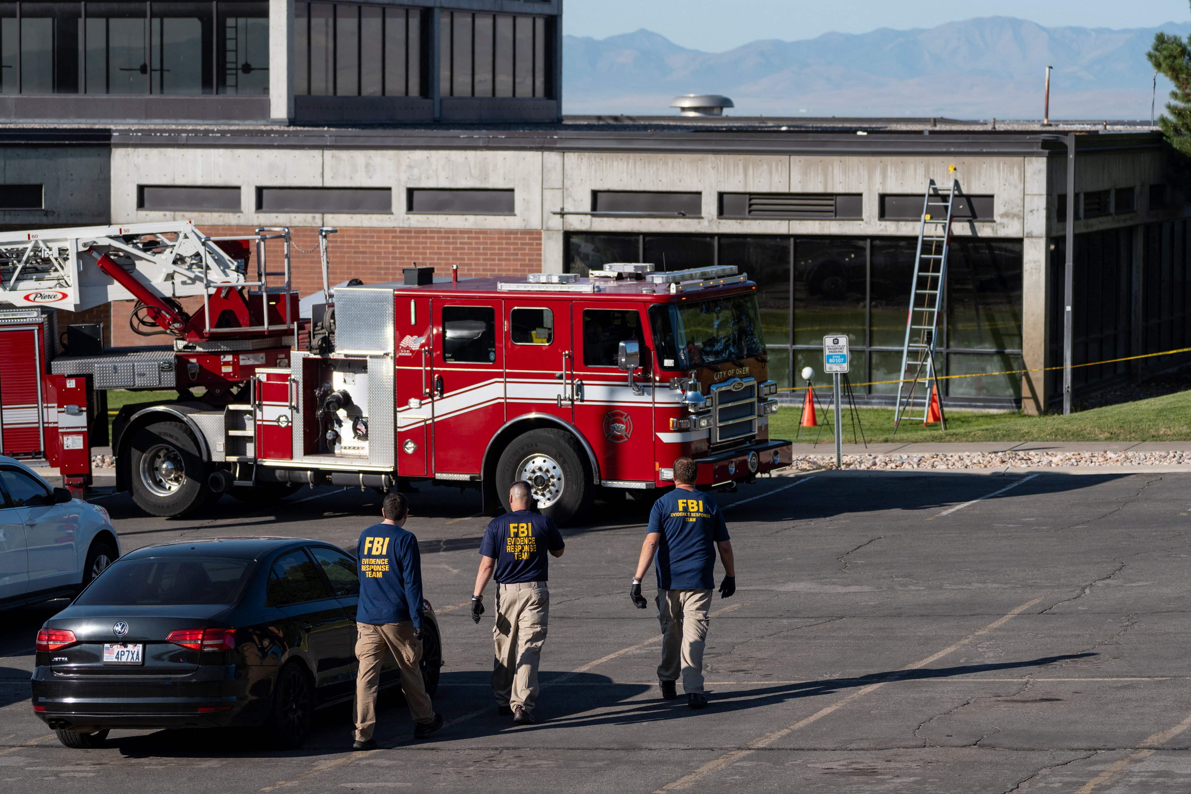 A ladder rests against a building. Three FBI agents walk towards it.