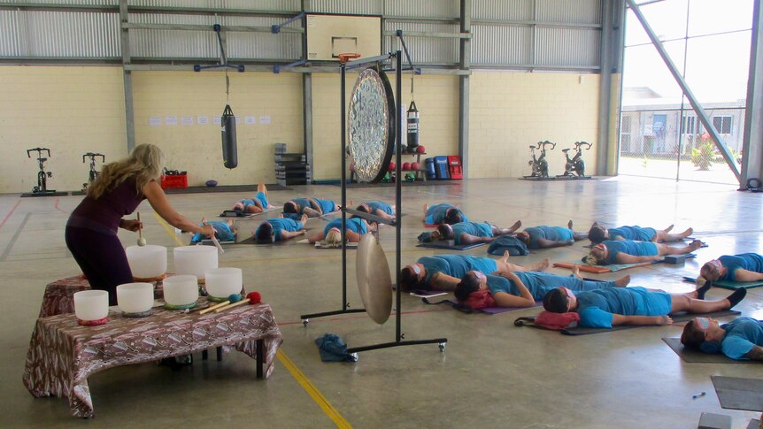 A yoga instructor takes a yoga class with 22 incarcerated women lying on the floor on yoga mats.