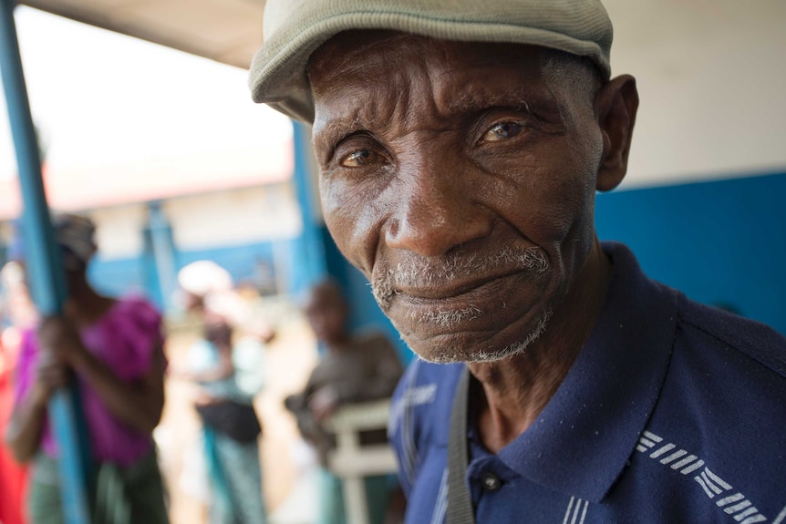 A close-up of a DRC man with light white stubble and a pale green hat.
