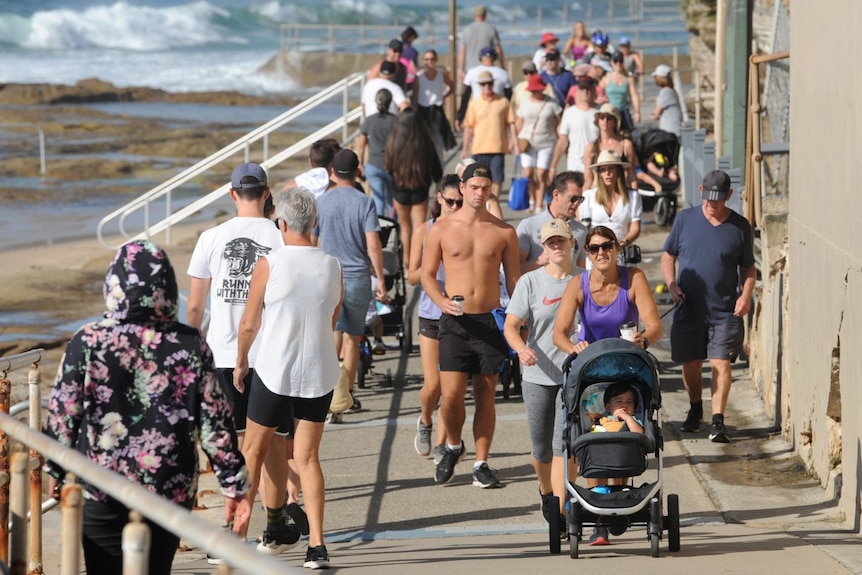 Crowds of people walk along a promenade at a beach.