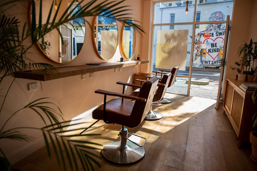 Three empty chairs, facing a wall adorned with mirrors.