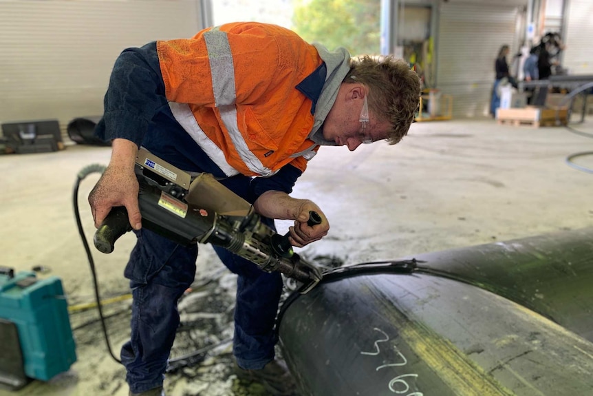 A man uses a large tool to cut plastic in a factory.