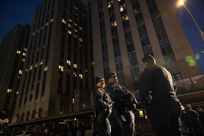 Three NYPD officers standing outside a Manhattan building at night