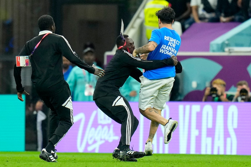 A referee grabs a protestor on a soccer field