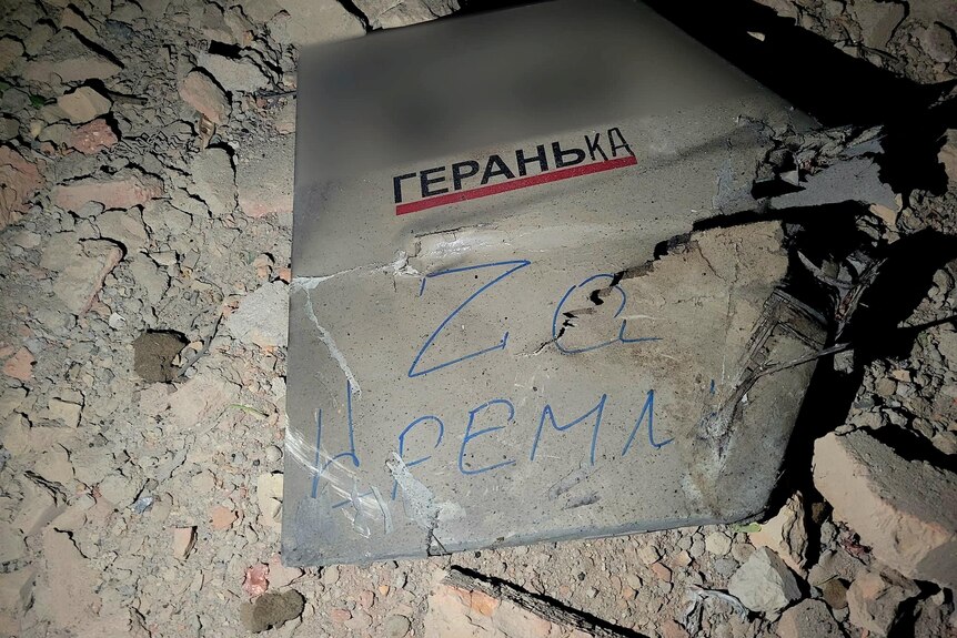 A grey part of a drone is pictured with Russian lettering on it, underneath it is rubble. 