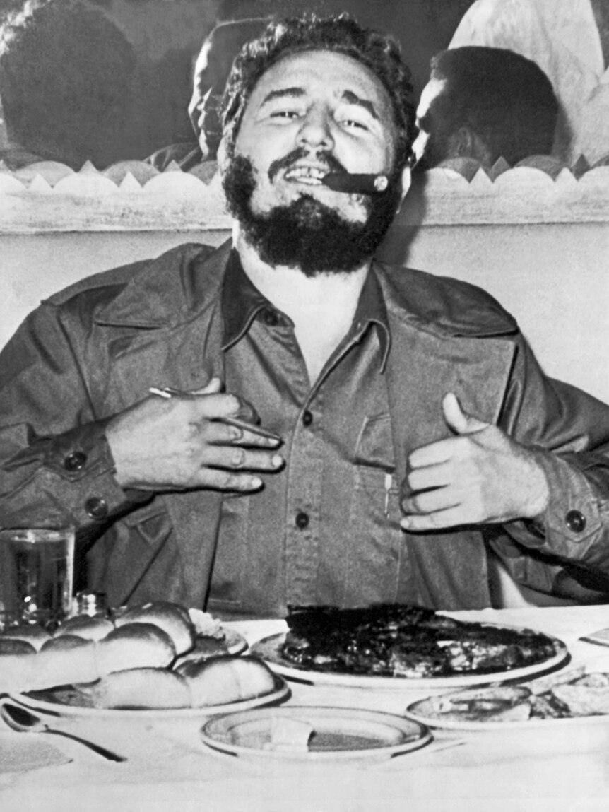 Black and white photo of Fidel Castro eating a steak during a press conference in 1960.