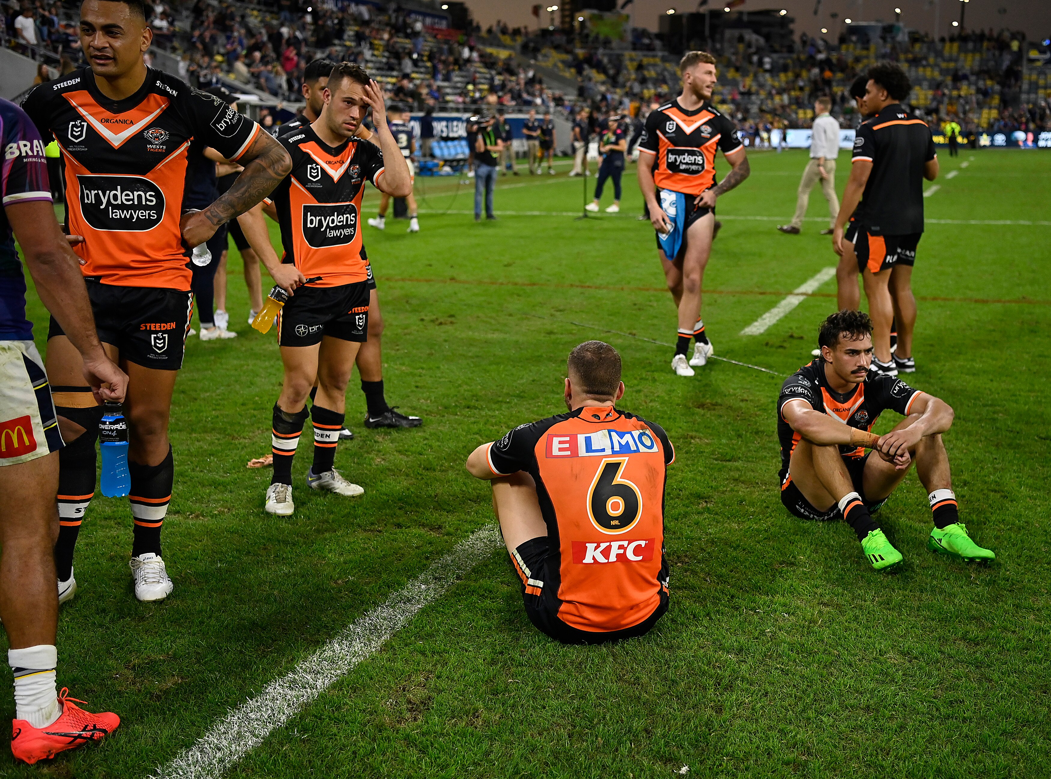 A group of Wests Tigers stand around looking abandoned or sit on the ground with their hands on their knees.