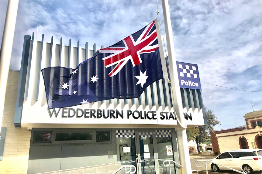 An Australian flag is flown at half mast on a cloudy day outside a police station.
