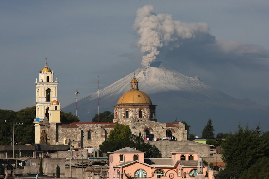 A church building with a volcano spewing ash in the background. 