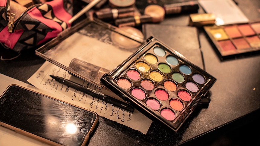 Close-up photo of make-up eye shadow palette on dressing room table top next to iPhone, pen and paper notes.