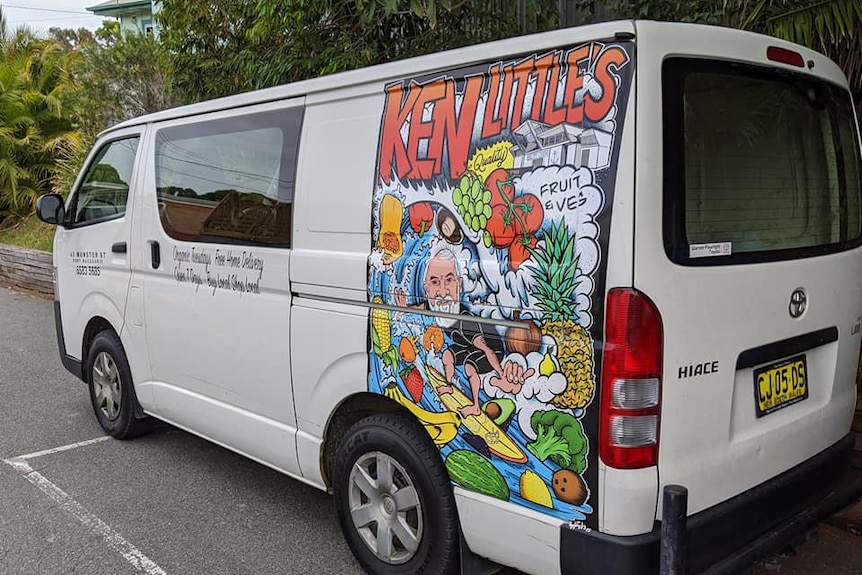 A brightly coloured mural depicting a surfer surrounded by fruit and vegies on the side of a white van