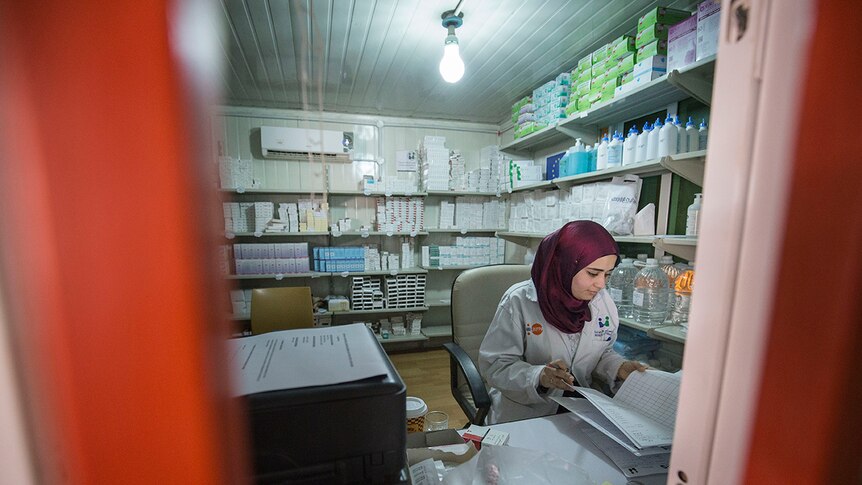 Dr Rima Diab sits at her desk surrounded by shelves with medical supplies.