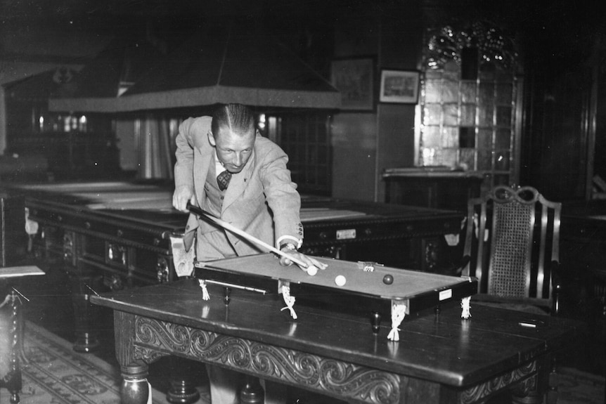 A man plays billiards on a miniature table.