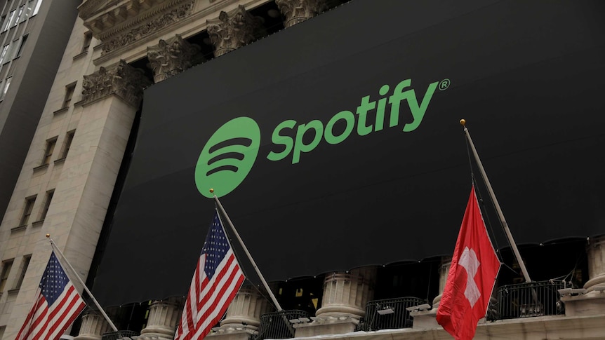 The Spotify logo hangs on the facade of the New York Stock Exchange with US and a Swiss flag