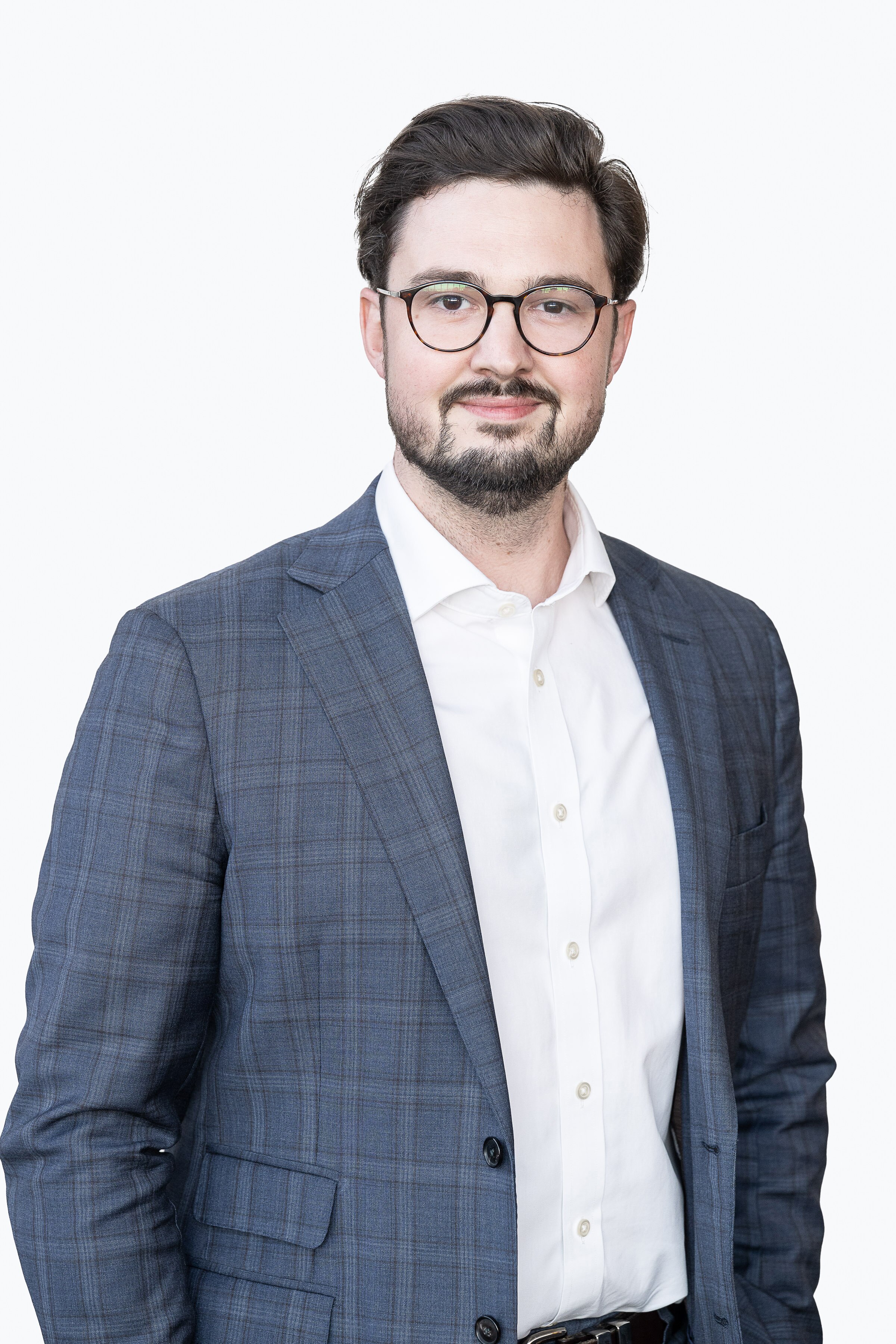 A man in a dark grey suit with a beard smiling for the camera