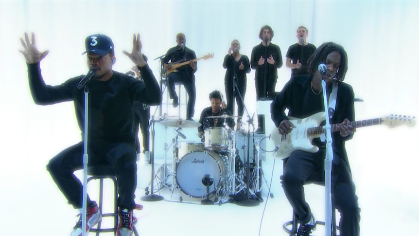 Chance the Rapper performs in black in front of his band on a luminescent white background