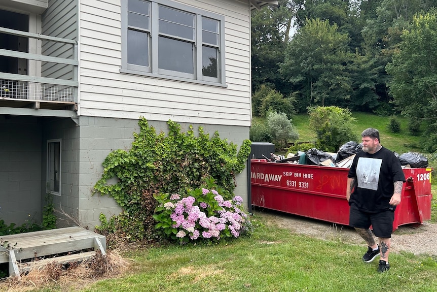 A man in a black shirt walks in the front garden of a house