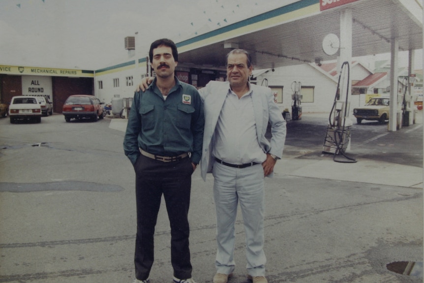 An old photograph of two men in front of a service station, one has his arm around the other