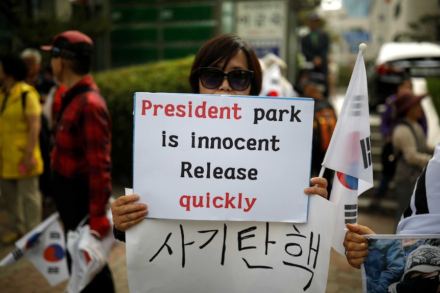 A woman holds a sign which says 'President Park is innocent - release quickly'