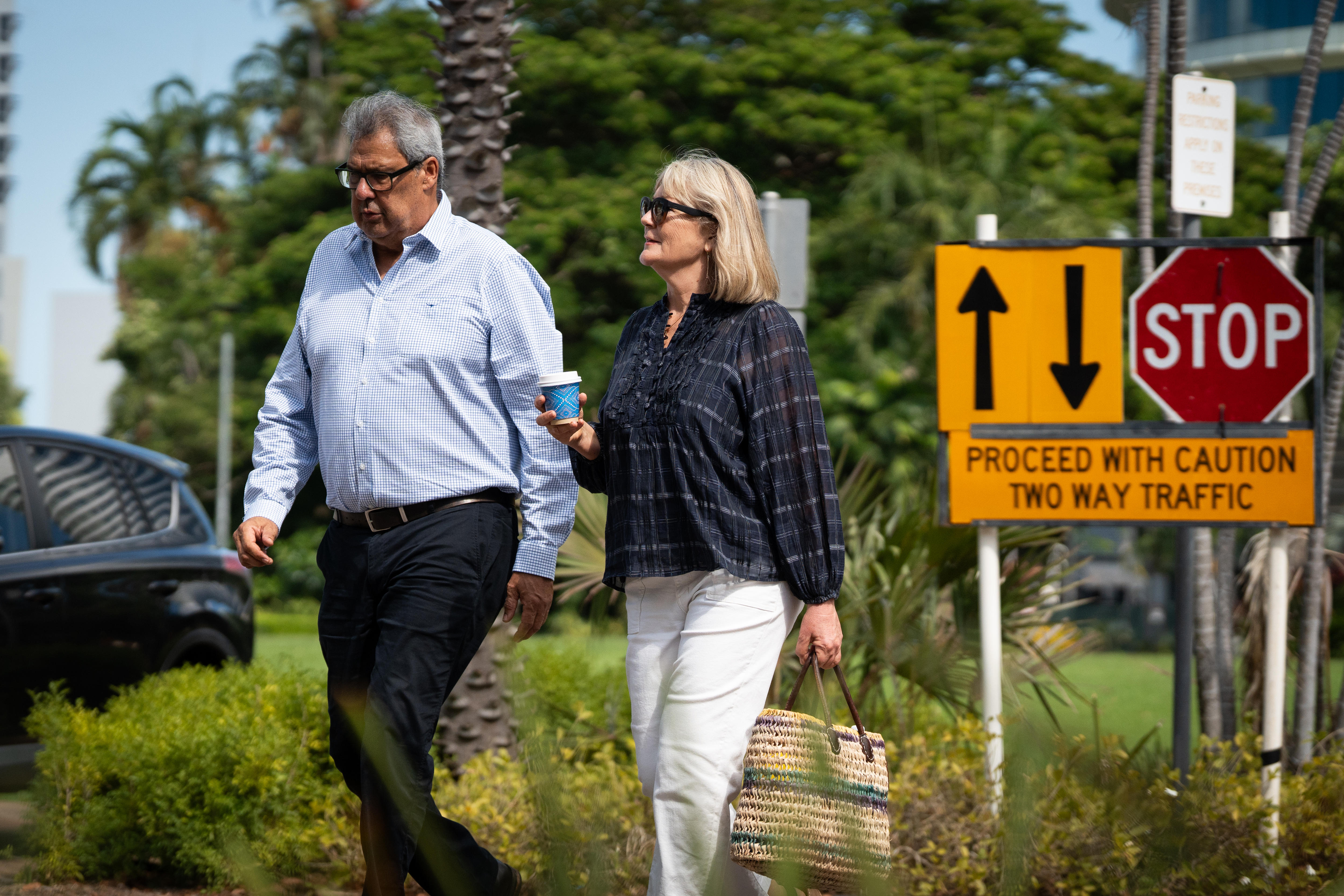 Um homem andando com sua esposa usa óculos de leitura e sua esposa usa óculos escuros.