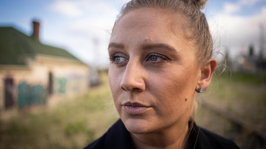 Woman with her hair up in a bun, outside in a field, looking away from the camera.