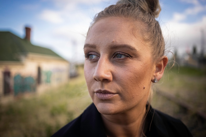 Woman with her hair up in a bun, outside in a field, looking away from the camera.