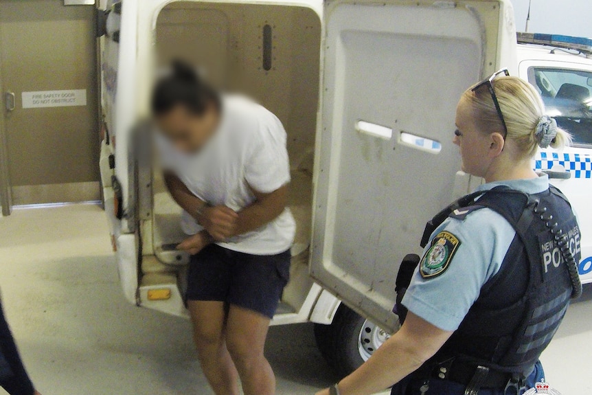 A man exits a police van in handcuffs