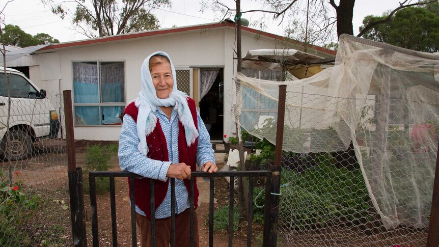 A woman stands outside a fibro house