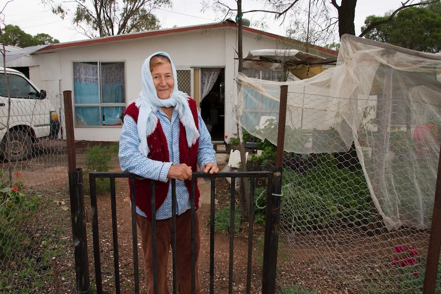 A woman stands outside a fibro house