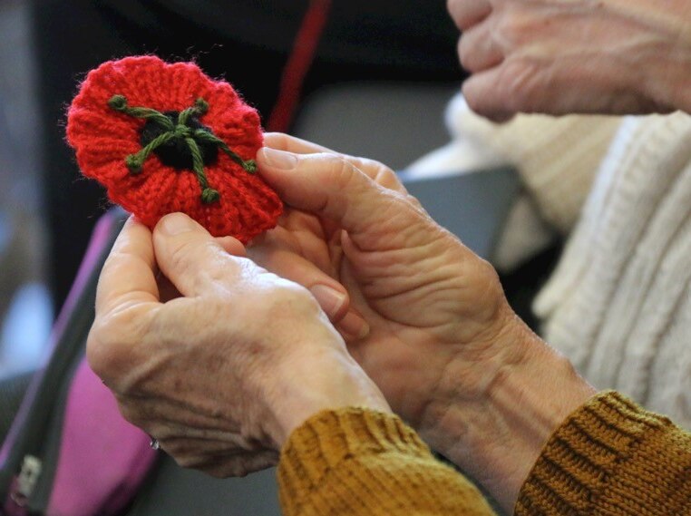 A woman's hands hold a decorative red poppy she has knitted.