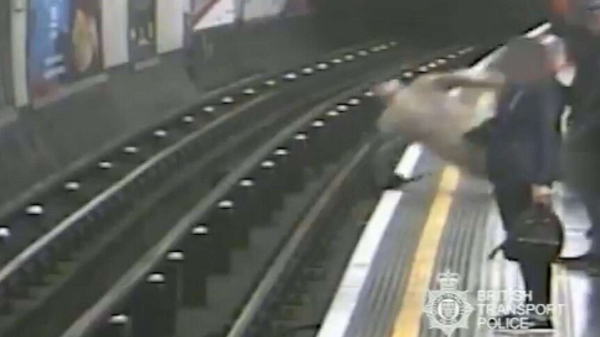 As commuters stand waiting on a platform, one figure falls towards the tracks